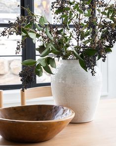 a white vase sitting on top of a wooden table next to a bowl filled with flowers