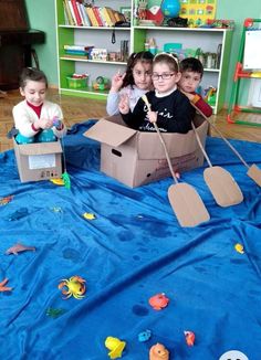 children playing with cardboard boats on a blue blanket in a play room at the school