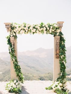 the wedding arch is decorated with white flowers and greenery