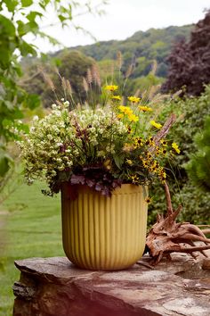 a yellow vase filled with flowers sitting on top of a wooden table next to a lush green field