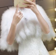 a woman taking a selfie in front of a mirror wearing a white fur coat