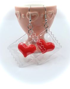 This listing is for one pair of clear candy wrapper dangle earrings with sweet little red heart "candy" tucked inside.  *Lightweight, soft plastic resin with hypoallergenic silver plated stainless steel ear wire hooks; rubber push stopper backs included.  *Approximately 2 inch drop length and weighing less than 1 gram/earring.    Stop by and say hi!  www.facebook.com/CrossMyHeartCo/ www.instagram.com/Cross.My.Heart.Co ✨ All thoughts, feelings, beliefs, and opinions found here are my own and are Red Heart-shaped Novelty Jewelry, Valentine's Day Clear Jewelry For Party, Novelty Red Resin Jewelry, Red Resin Novelty Jewelry, Red Plastic Earrings For Gift, Sweet Red Jewelry For Valentine's Day, Novelty Heart-shaped Earrings For Gift, Sweet Dangle Heart Earrings For Gifts, Clear Plastic Jewelry For Gifts