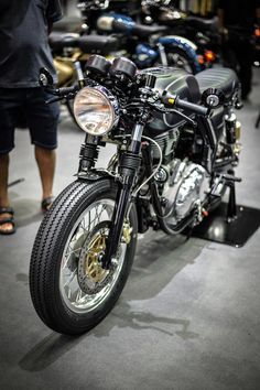 a black motorcycle parked on top of a gray floor next to other motorcycles and people