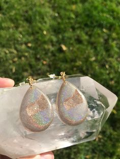 These holographic Teardrop geode earrings made from resin shift from clear gold to a beautiful sparkly rainbow. They are lightweight and won't bother your ears. Please be aware that resin is heat resistant up to 135 degrees. Wearing these earrings in extremely hot temperatures will cause them to be pliable. If this happens, simply place in a cooler location. I am not responsible for any damaged earrings due to extreme heat. Made by Katie Glover Resin Art by Katie 2020 Contact me on my Instagram Iridescent Hypoallergenic Drop Earrings, Iridescent Sparkling Dangle Earrings, Sparkling Iridescent Dangle Earrings, Unique Iridescent Teardrop Earrings, Gold Hypoallergenic Drop Crystal Earrings, Glitter Teardrop Earrings For Gifts, Glitter Teardrop Earrings As Gift, Silver Glitter Teardrop Earrings, Hypoallergenic Gold Drop Crystal Earrings