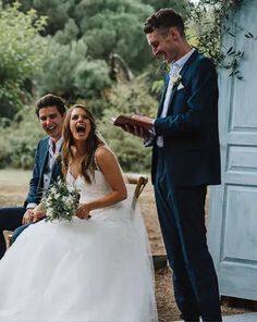 a bride and groom laugh as they sit on a bench in front of an open door