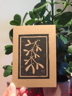 a hand holding up a card with an image of a plant in the background and a potted plant behind it