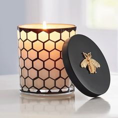 a candle with a bee on it sitting next to a black container that has a honeycomb design