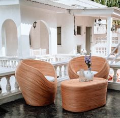 two wicker chairs and a table in front of a white house with flowers on it