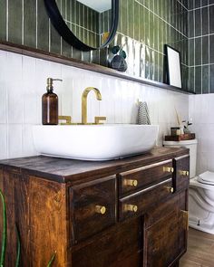 a white sink sitting on top of a wooden cabinet next to a toilet and mirror