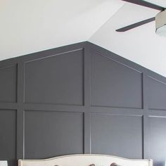 a white bed sitting in a bedroom next to a ceiling fan on top of a wooden headboard