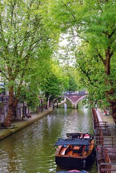 two boats are docked on the side of a canal in an urban area with trees lining both sides