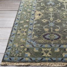 a green rug with blue and yellow designs on it sitting on a wooden floor next to a window