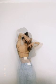 a woman standing in front of a white wall with her back to the camera and arms behind her head