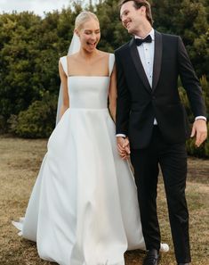 a bride and groom holding hands walking through the grass