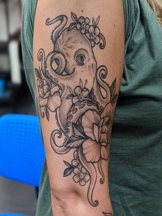 an octopus tattoo on the arm and shoulder with flowers around its neck, in front of a woman's green t - shirt