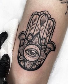 a black and white hamsa tattoo with an eye in the center on someone's leg