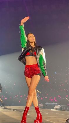 a woman in red and green outfit on stage with her arms up to the side