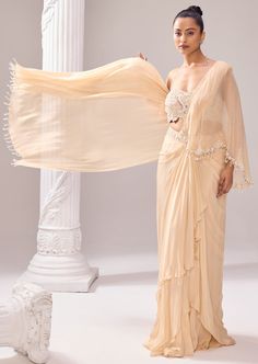 A drape saree in muted beige hues allured with intricate embroidery on a tube blouse with a halter neck beaded strap. There is a cascade drape attached from the belt, falling free from the front. The distinctive artwork with ethereal detailing in the blouse and hemline of the cape exhibits impeccable couture craftsmanship. The ensemble is further highlighted with tassels all over the pallu and cascade. Silk Draped Dupatta For Reception, Tissue Silk Pre-draped Saree For Wedding, Elegant Draped Cutdana Blouse Piece, Elegant Draped Blouse Piece With Cutdana, Pre-draped Tissue Silk Saree For Wedding, Draped Tissue Silk Lehenga, Embellished Silk Pre-draped Saree, Embellished Pre-draped Silk Saree, Formal Pre-draped Saree With Sheer Dupatta