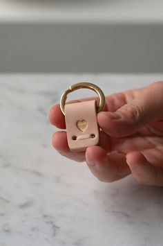 a person holding a ring with a heart on it in their left hand and the other hand has a small keychain attached to it