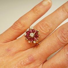 Here we have a gorgeous earth mined red ruby and sparkly white diamond 1950s ring in 14K yellow gold.This exceptional floral ring is gorgeous from every angle you view it- it's like a small wearable sculpture. The gem quality rubies are beautifully matched for color throughout. There are 0.81 carats of fine gem rubies. In total the diamond accents weigh 0.34 carats. These pretty diamonds are SI clarity and J in color. The total precious ruby and diamond weight here is 1.15 carats. Inside the sha Cluster Ruby Rings With Diamond Accents, Ruby Cluster Rings With Diamond Accents, Diamond Cluster Ruby Ring With Diamond Accents, Cluster Ruby Ring With Diamond Accents, Cluster Ruby Diamond Ring With Center Stone, Fine Jewelry Ruby Cluster Ring With Diamond Accents, Cluster Ruby Ring With Diamond Accents As Gift, Cluster Ruby Ring With Diamond Accents For Gift, Ruby And Diamond Cluster Promise Ring