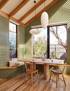 a dining room with green walls and wooden flooring, along with two windows that look out onto the backyard