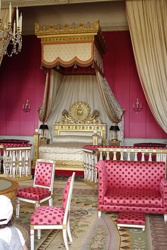 an ornate bedroom with pink and gold furniture, chandelier, fireplace and mirror