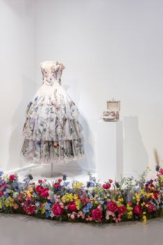 a dress on display in a white room with flowers around the neck and bottom part