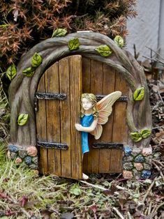 a fairy figurine sitting on top of a wooden door in the middle of grass