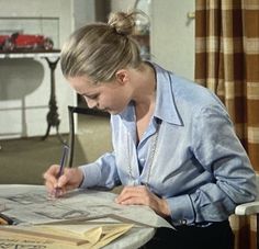 a woman sitting at a table writing on a piece of paper with a pencil in her hand