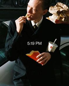 a man in a suit eating food next to a car with the caption 5 19 pm