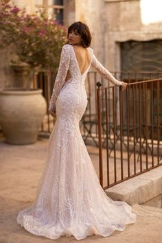 a woman in a long sleeved wedding dress standing next to a fence with her back turned towards the camera