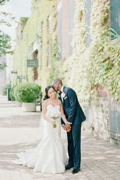 a bride and groom pose for a photo in front of an old brick building with ivy growing on it