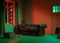 a person sitting on a couch in front of a neon sign that reads chica