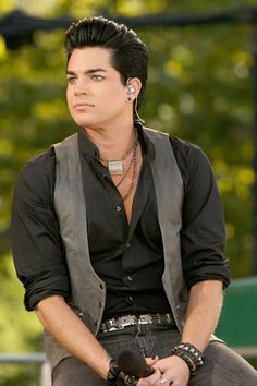 a man sitting on top of a bench wearing a black shirt and gray vest with ear phones in his ears