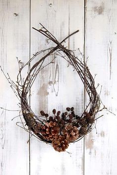 a wreath with pine cones and branches hanging on a white wooden wall next to scissors