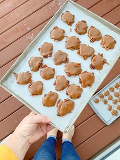 a person holding a tray full of cookies on top of a wooden table next to a cookie sheet