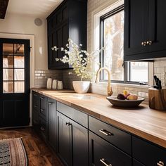 a bowl of fruit is on the counter in this black and white kitchen with wood flooring