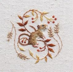 a small embroidered mouse sitting on top of a white piece of cloth with leaves and berries