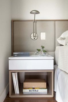 a nightstand with books and a lamp on top of it in a small room next to a bed