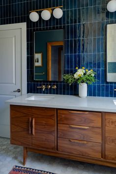 a bathroom with blue tiles and wooden cabinets, two sinks and a large mirror on the wall