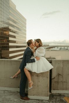 a bride and groom kissing on the roof of a building in front of a cityscape