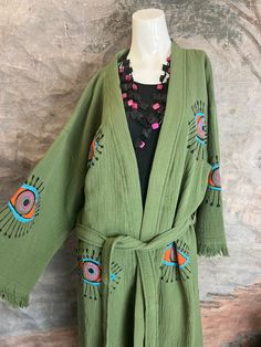 41023 Evil Eye Kimono Robe. How fun are these!!! We have more colors and prints coming soon. This olive-hued, handmade kimono-style robe is crafted from 100% organic cotton, and emblazoned with an all-seeing evil eye motif. With its gender-neutral design, it's a versatile, protective cover-up for the beach, the spa, festivals, or any time you want to bring a casual look to the next level. It's believed that the evil eye will keep wearers safe from negative energy and carry luck in other areas of Cotton Open Front Kimono For Fall, Fall Cotton Open Front Kimono, Cotton Kimono For Fall Loungewear, Cotton Kimono For Loungewear In Fall, One Size Green Kimono For Festival, Bohemian Cotton Kimono For Fall, Green One Size Kimono For Festival, Green One-size Festival Kimono, Green Oversized Kimono For Spring