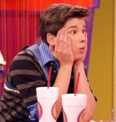 a young boy sitting at a table with two drinks in front of him and his hand on his face