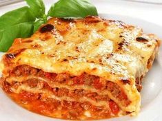 a white plate topped with lasagna covered in sauce and cheese next to a green leaf