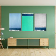 three abstract paintings hang on the wall above a wooden cabinet in a living room with green walls