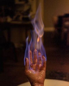 a hand holding something with flames coming out of the top and bottom of it, in front of a table