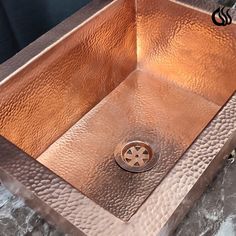 a square copper sink with a drain in the middle and a circular metal faucet