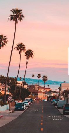 a street with cars parked on both sides and palm trees in the background at sunset