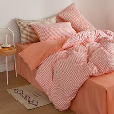 a bed with pink and white checkered comforter on it, next to a small table