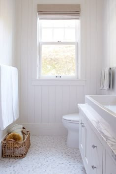 a white bathroom with a window, sink and toilet